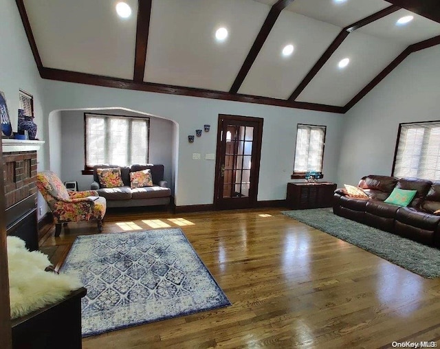 living room with beam ceiling, wood-type flooring, a wealth of natural light, and a brick fireplace