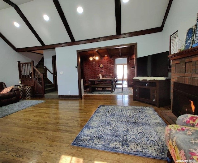 living room featuring a fireplace, brick wall, hardwood / wood-style flooring, beamed ceiling, and a chandelier