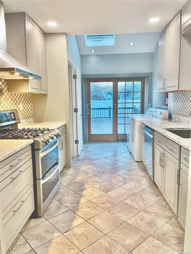 kitchen featuring light stone countertops, wall chimney exhaust hood, tasteful backsplash, independent washer and dryer, and appliances with stainless steel finishes