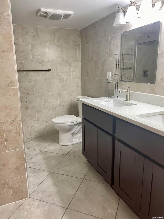 bathroom with tile patterned flooring, toilet, tiled shower, vanity, and tile walls