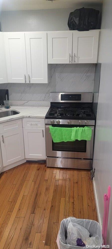 kitchen featuring decorative backsplash, light hardwood / wood-style floors, white cabinetry, and gas range