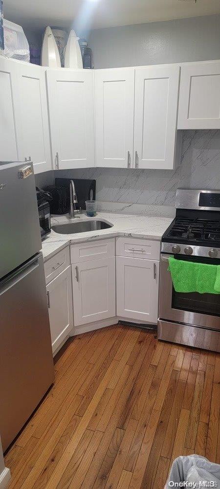 kitchen featuring appliances with stainless steel finishes, tasteful backsplash, sink, light hardwood / wood-style floors, and white cabinetry