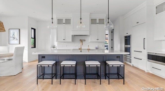 kitchen with white cabinetry, an island with sink, hanging light fixtures, and light hardwood / wood-style flooring