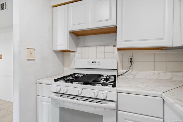 kitchen featuring light stone countertops, white gas range oven, backsplash, white cabinetry, and light tile patterned flooring