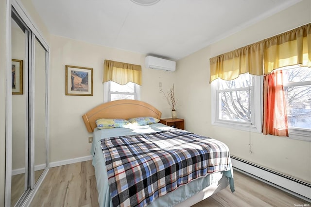 bedroom featuring baseboard heating, a closet, light hardwood / wood-style floors, and an AC wall unit