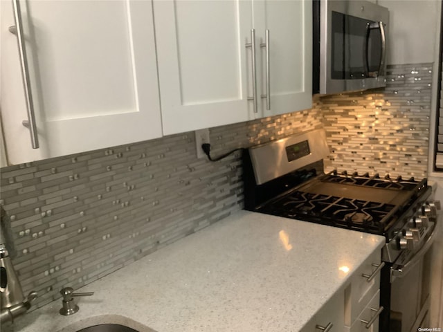 kitchen featuring decorative backsplash, light stone countertops, white cabinets, and stainless steel appliances