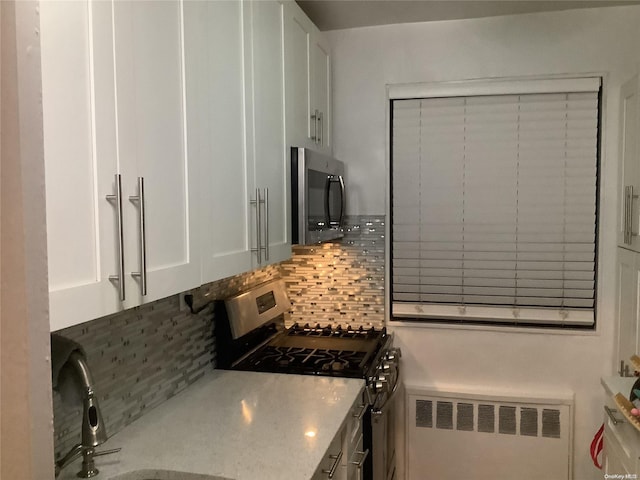 kitchen featuring radiator, white cabinets, sink, tasteful backsplash, and stainless steel appliances