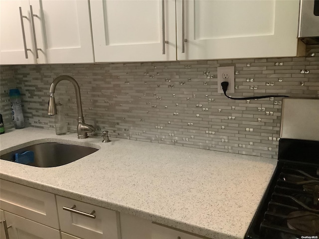 kitchen with backsplash, white cabinetry, light stone countertops, and sink