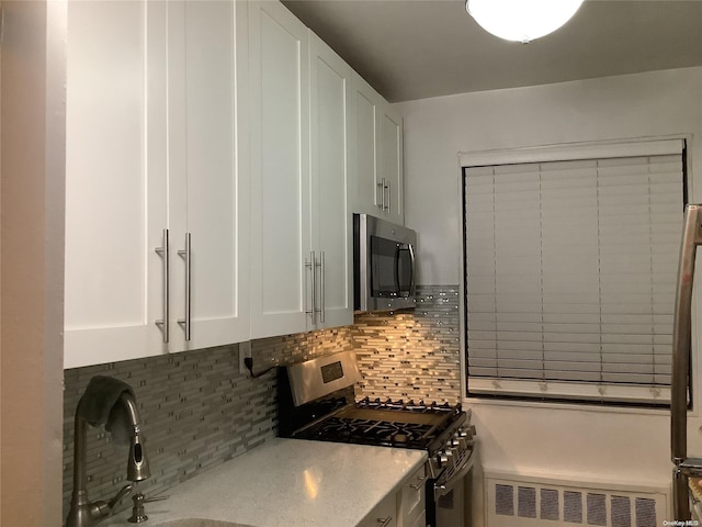 kitchen with decorative backsplash, appliances with stainless steel finishes, sink, white cabinets, and radiator heating unit