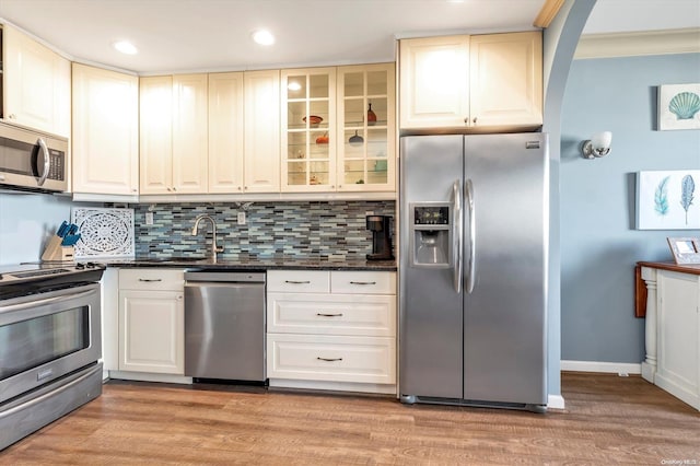 kitchen featuring tasteful backsplash, sink, dark stone counters, stainless steel appliances, and light wood-type flooring