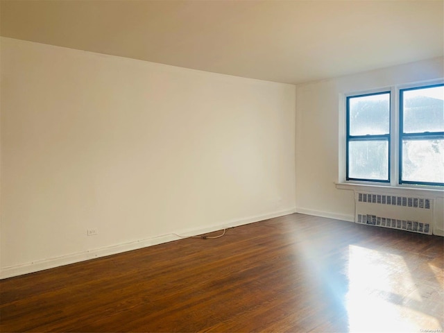 empty room with radiator heating unit and dark wood-type flooring