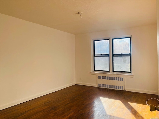 unfurnished room with dark hardwood / wood-style flooring and radiator