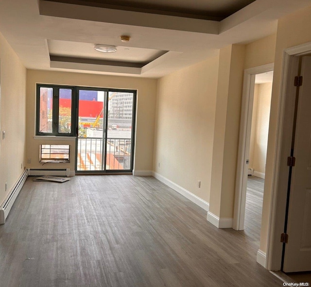 empty room with wood-type flooring, a tray ceiling, and baseboard heating