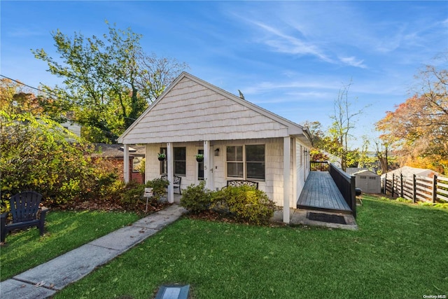 bungalow-style house featuring a storage unit, covered porch, and a front lawn