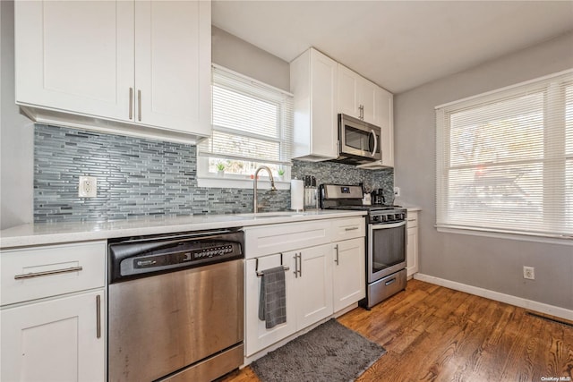 kitchen featuring decorative backsplash, wood-type flooring, stainless steel appliances, and white cabinetry