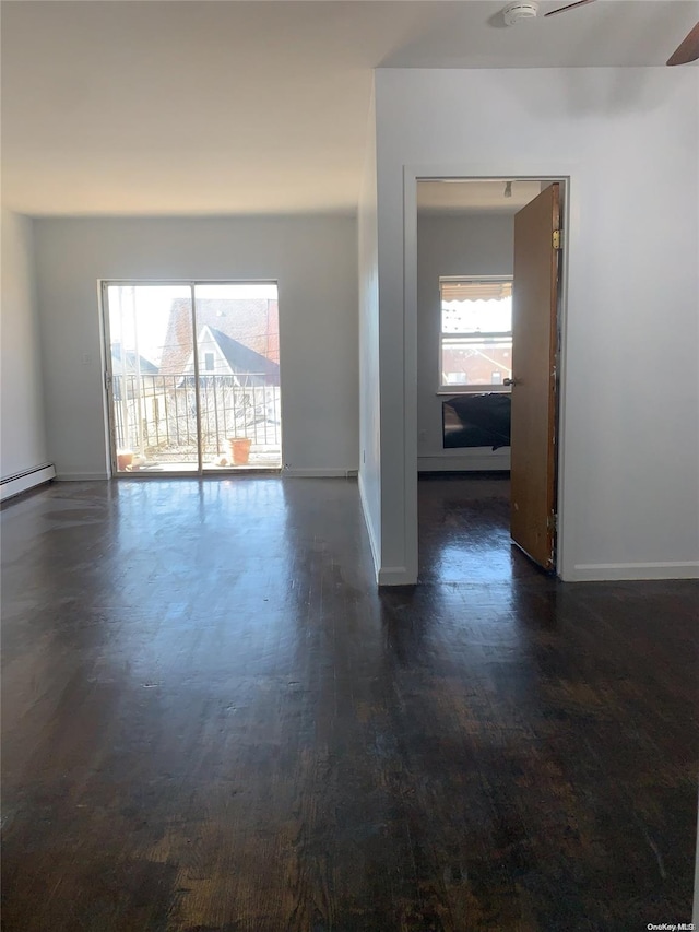 empty room with baseboard heating, ceiling fan, a healthy amount of sunlight, and dark hardwood / wood-style floors