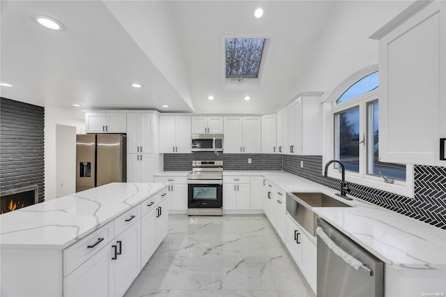 kitchen with light stone countertops, appliances with stainless steel finishes, a kitchen island, sink, and white cabinetry