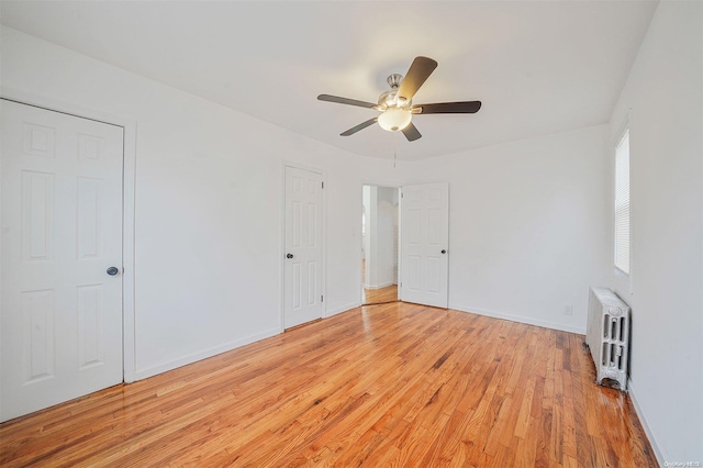 empty room featuring ceiling fan, radiator heating unit, and light hardwood / wood-style flooring