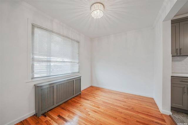 unfurnished dining area with a chandelier, radiator heating unit, light wood-type flooring, and crown molding