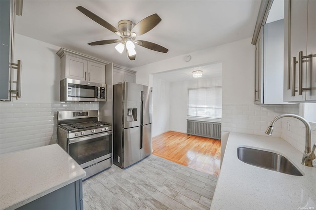 kitchen with appliances with stainless steel finishes, light wood-type flooring, tasteful backsplash, radiator, and sink