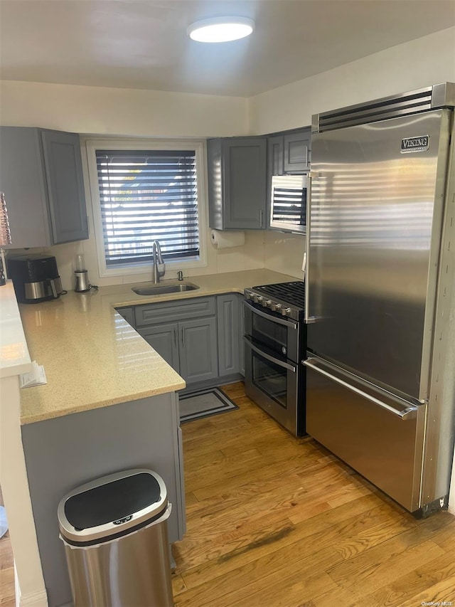 kitchen with sink, light stone counters, light hardwood / wood-style flooring, gray cabinets, and appliances with stainless steel finishes