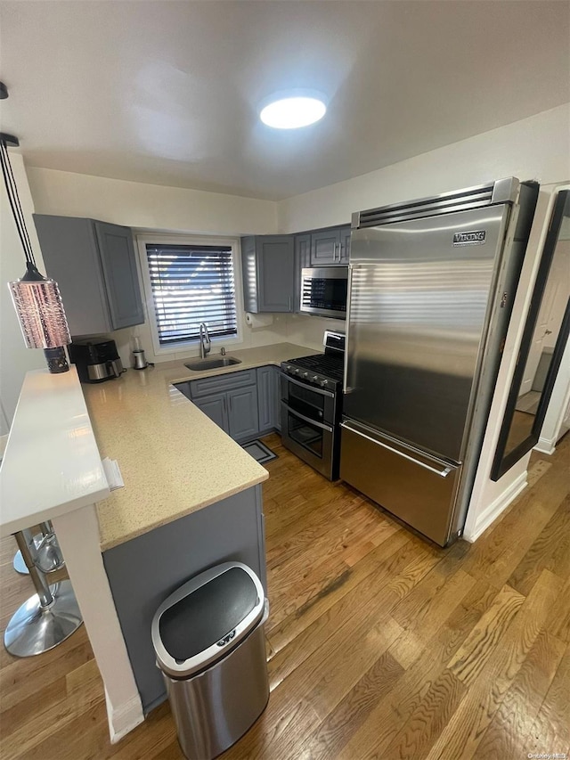 kitchen with light wood-type flooring, gray cabinetry, stainless steel appliances, sink, and decorative light fixtures