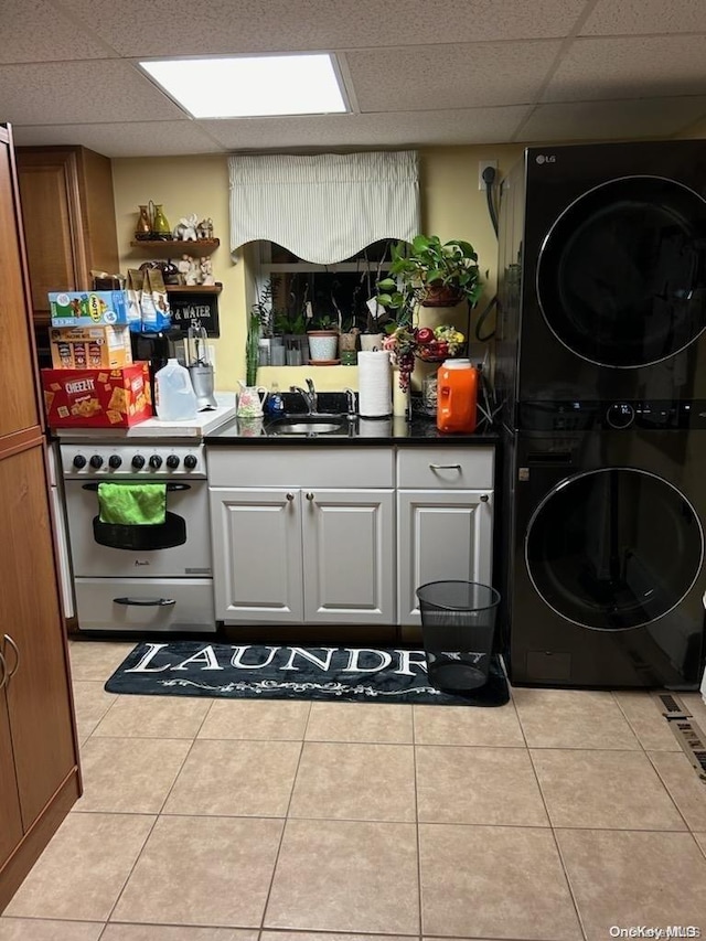 kitchen featuring a paneled ceiling, light tile patterned flooring, stacked washer and clothes dryer, and range