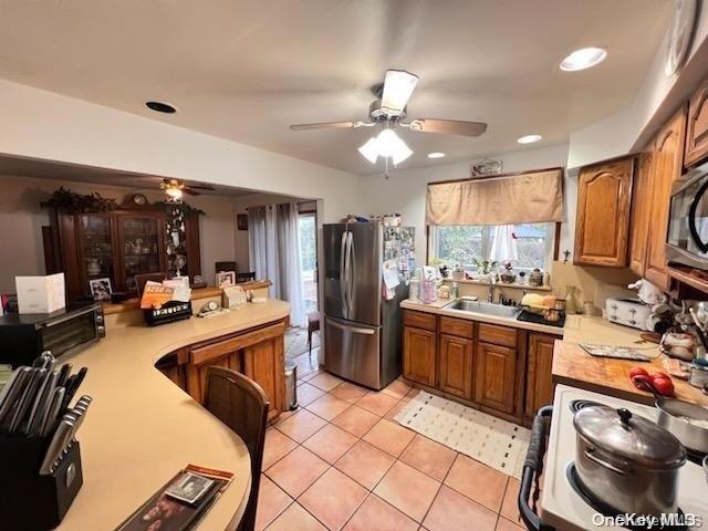 kitchen with ceiling fan, sink, stainless steel appliances, kitchen peninsula, and light tile patterned floors