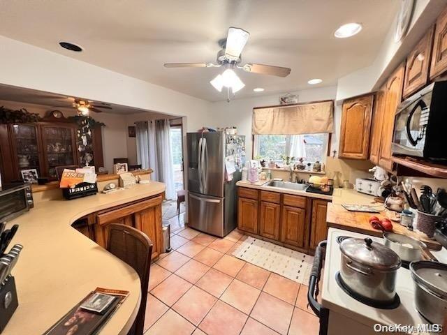 kitchen with ceiling fan, sink, kitchen peninsula, light tile patterned floors, and appliances with stainless steel finishes