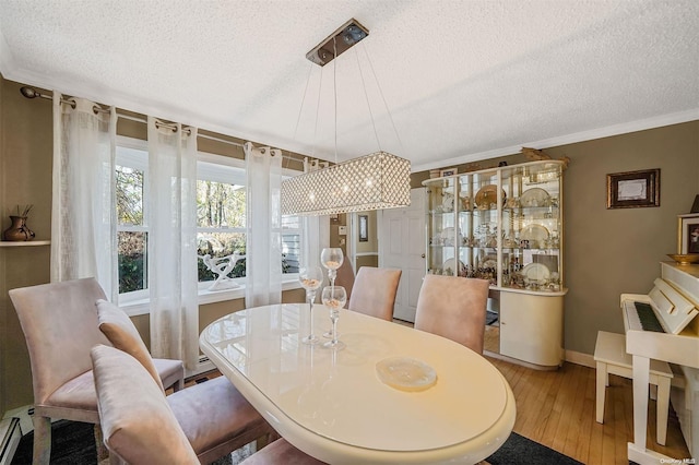 dining area featuring a textured ceiling, a baseboard heating unit, crown molding, and light wood-type flooring