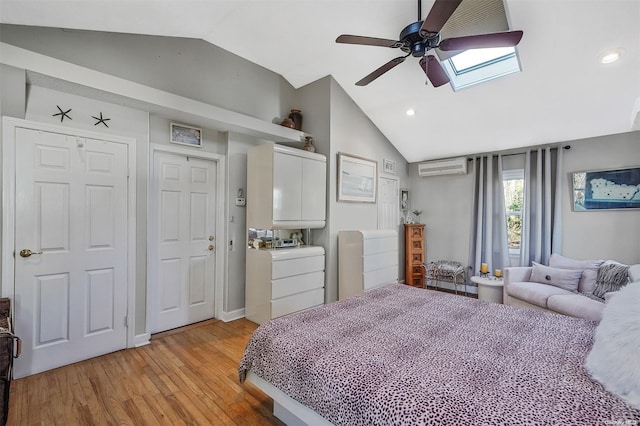 bedroom with ceiling fan, a wall mounted AC, light hardwood / wood-style flooring, and vaulted ceiling with skylight