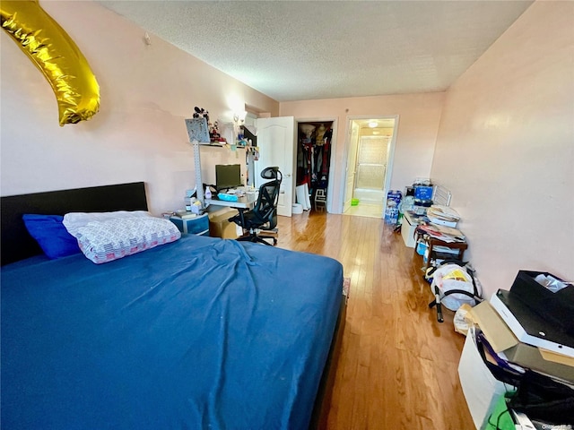 bedroom with a textured ceiling, hardwood / wood-style flooring, a spacious closet, connected bathroom, and a closet