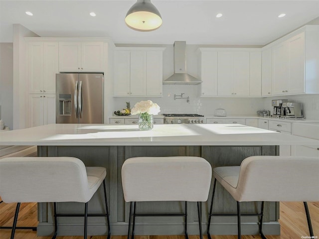 kitchen featuring stainless steel refrigerator with ice dispenser, white cabinetry, a center island, and wall chimney range hood