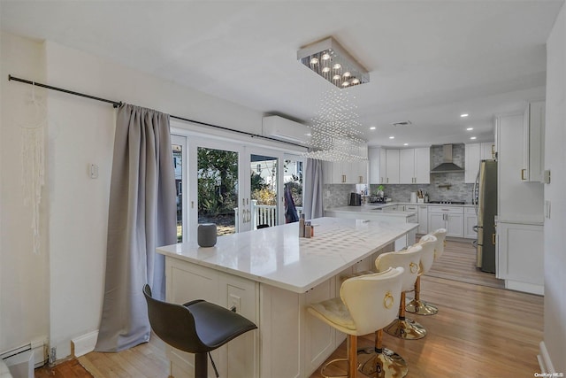 kitchen featuring white cabinetry, wall chimney exhaust hood, a baseboard radiator, light hardwood / wood-style flooring, and stainless steel fridge