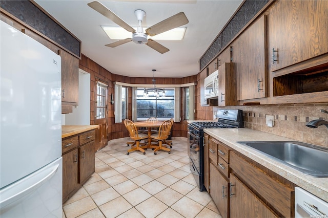 kitchen featuring decorative backsplash, white appliances, ceiling fan with notable chandelier, sink, and hanging light fixtures