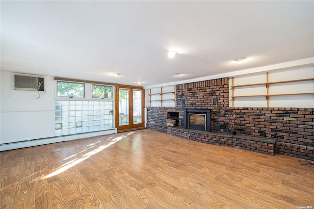 unfurnished living room with a brick fireplace, light wood-type flooring, baseboard heating, a wall mounted AC, and brick wall