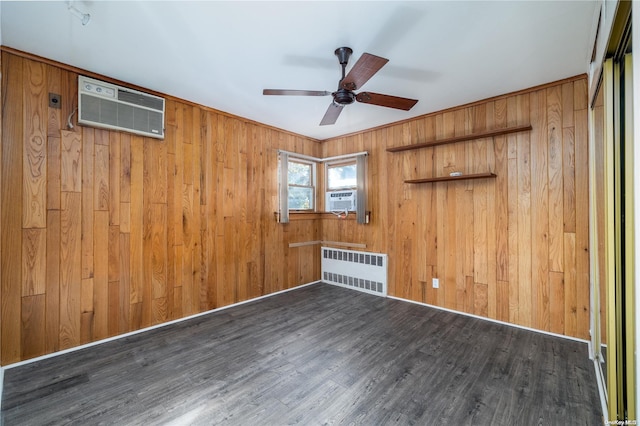 unfurnished room featuring dark hardwood / wood-style flooring, ceiling fan, a wall mounted AC, radiator heating unit, and wood walls