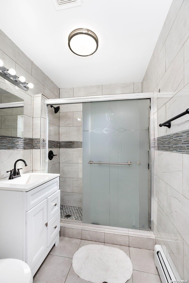 bathroom with baseboard heating, tile patterned flooring, an enclosed shower, vanity, and tile walls