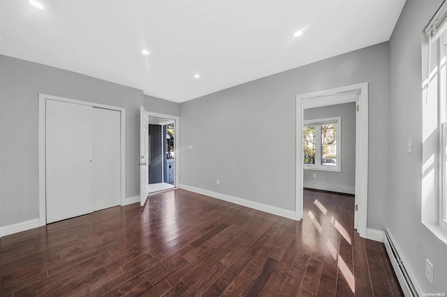 unfurnished bedroom featuring a closet, dark hardwood / wood-style flooring, and a baseboard heating unit