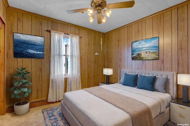 carpeted bedroom with ceiling fan, wooden walls, and crown molding