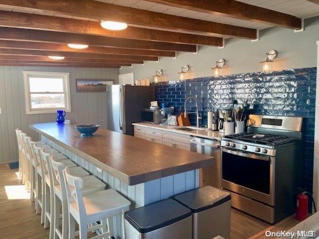 kitchen featuring sink, stainless steel appliances, light hardwood / wood-style floors, a kitchen bar, and wooden walls