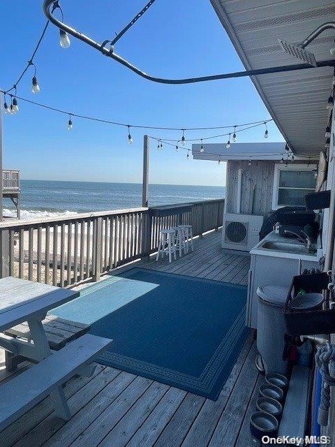 wooden terrace with a view of the beach, ac unit, and a water view