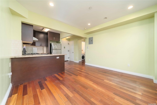 kitchen with backsplash, dark hardwood / wood-style floors, stainless steel fridge, dark brown cabinetry, and washer / clothes dryer