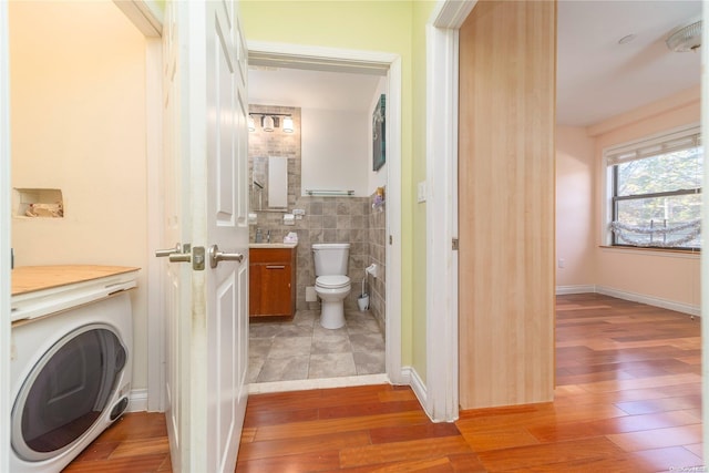 bathroom with vanity, wood-type flooring, tile walls, washer / dryer, and toilet