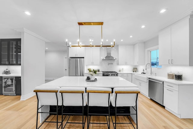 kitchen with a center island, wall chimney range hood, sink, stainless steel appliances, and beverage cooler