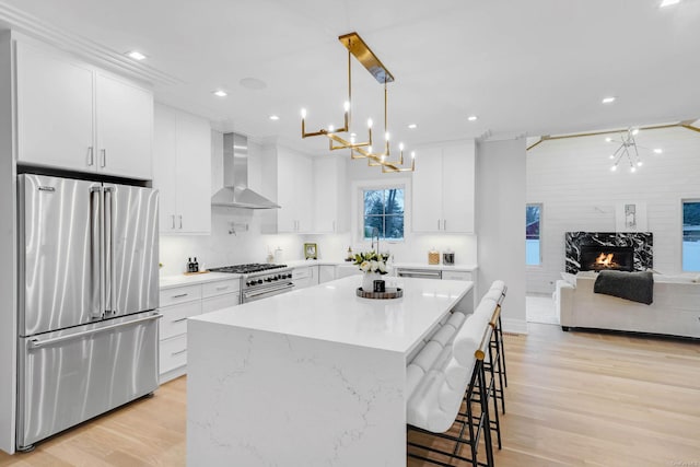 kitchen featuring wall chimney exhaust hood, high end appliances, white cabinetry, and decorative light fixtures