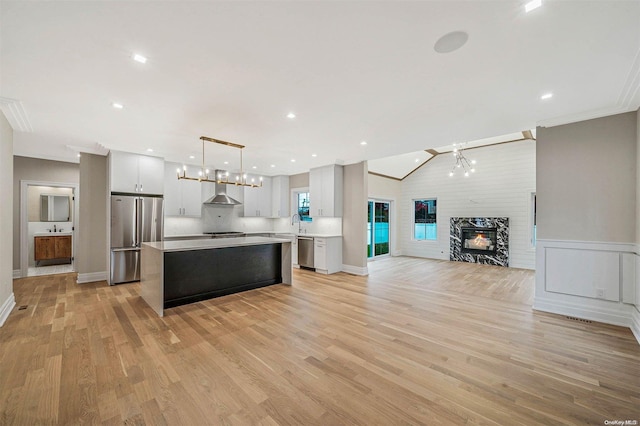 kitchen featuring appliances with stainless steel finishes, light wood-type flooring, wall chimney range hood, a fireplace, and hanging light fixtures