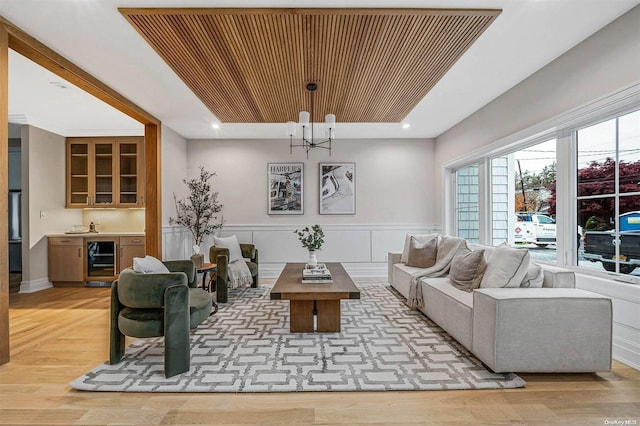 living room with bar, light hardwood / wood-style floors, wine cooler, and an inviting chandelier