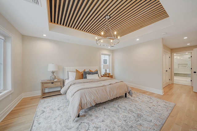 bedroom featuring a tray ceiling, ensuite bathroom, a chandelier, and light hardwood / wood-style floors