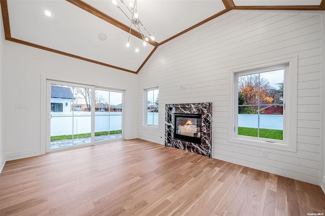 unfurnished living room with a high end fireplace, crown molding, high vaulted ceiling, light hardwood / wood-style floors, and wood walls